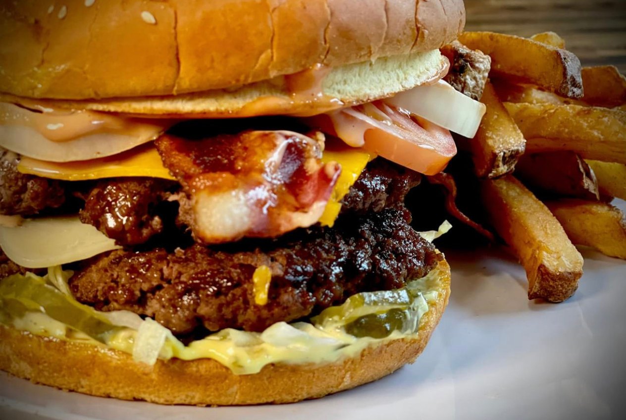 A tall double cheeseburger with bacon, onion and pickles, served with a pile of fries