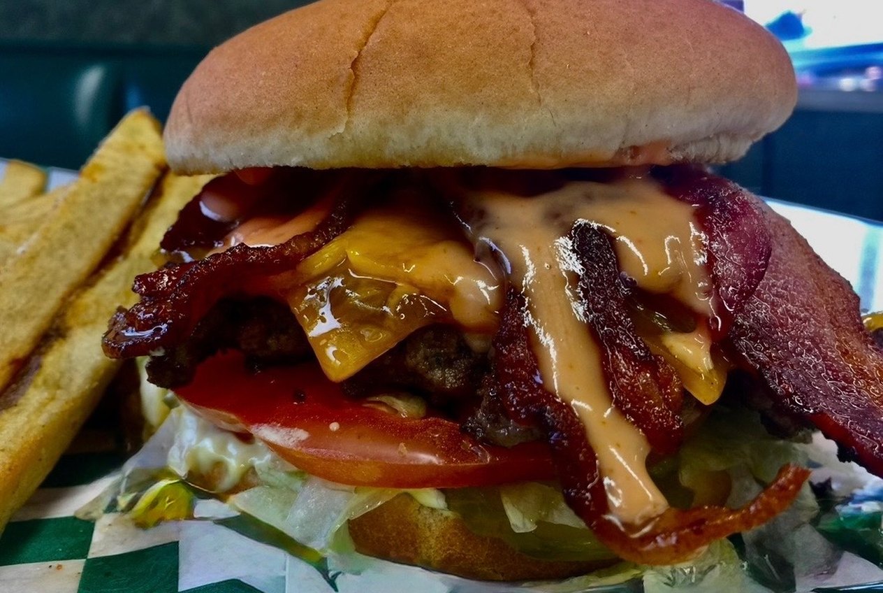 A stacked cheeseburger with bacon, melted cheese, tomato and sauce running down the side, on green checked paper