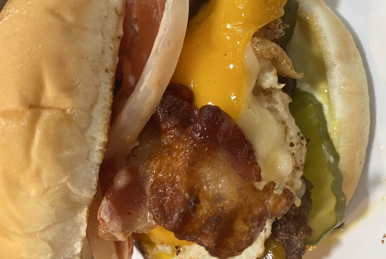 A close-up of a burger with bacon, melted cheese and pickles in a soft bun